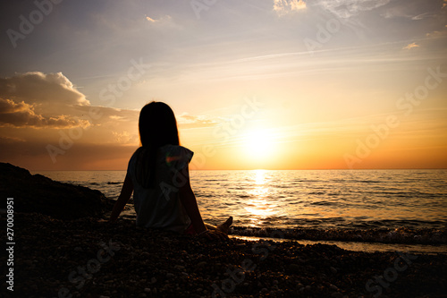 silhouette of a young girl. sits and watches the beautiful sunset on the sea.