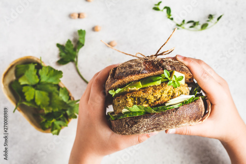 Vegan sandwich with chickpea patty, avocado, cucumber and greens in rye bread in children's hands. photo