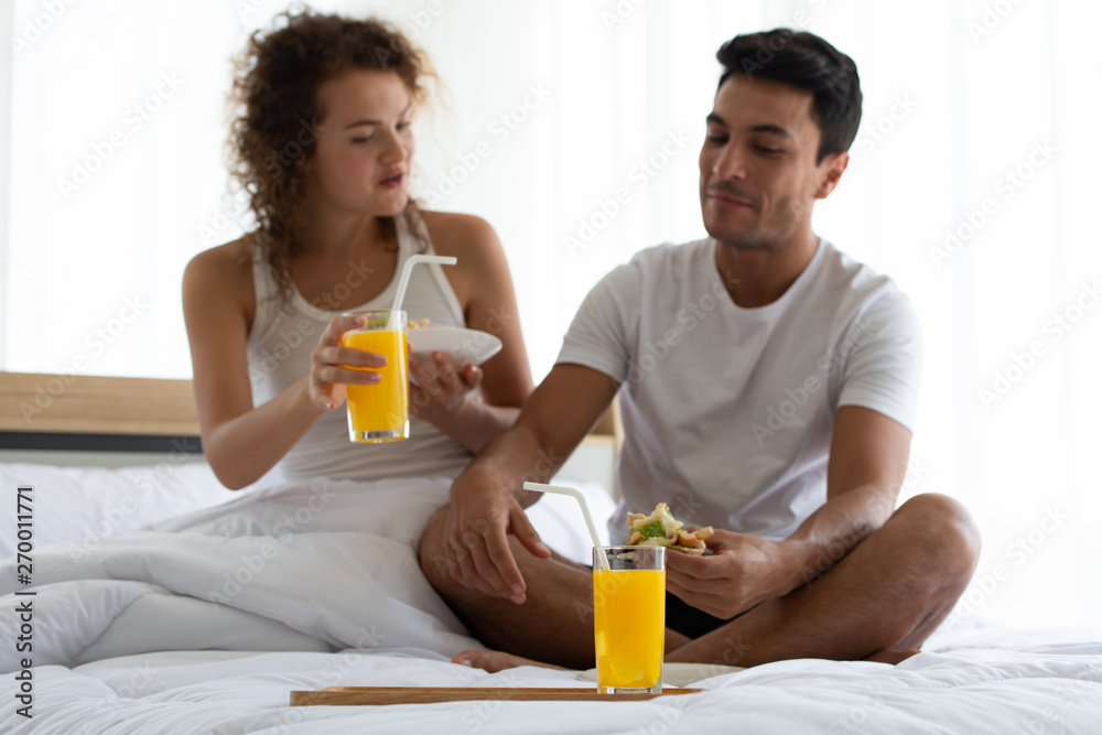 Happy couples relaxing in the white bedroom Of the apartment With various emotions With snacks, coffee, fruit in the morning Happy couples relaxing in the white bedroom Of the apartment With various emotions With snacks, coffee, fruit in the morning