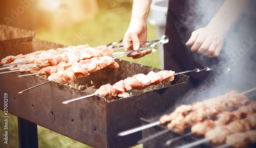 The chef prepares kebabs on metal skewers on the grill in the summer outdoors on a Sunny day.