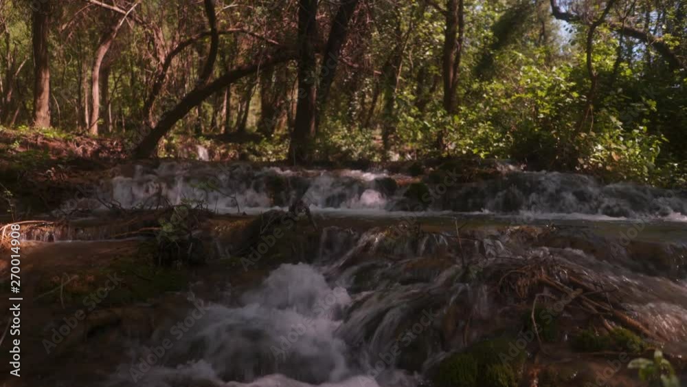 Ascending from low angle shot across cascading small waterfalls within Krka National park creek. Surrounded by shaded woodland trees & foliage. Ascending from low angle shot across cascading small waterfalls within Krka National park creek. Surrounded by shaded woodland trees & foliage.