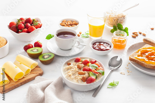 healthy breakfast with oatmeal porridge, strawberry, nuts, toast, jam and tea
