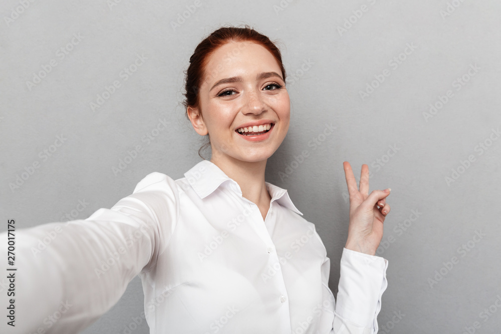 Image of happy redhead businesswoman 20s in formal wear smiling at camera while taking selfie photo Image of happy redhead businesswoman 20s in formal wear smiling at camera while taking selfie photo