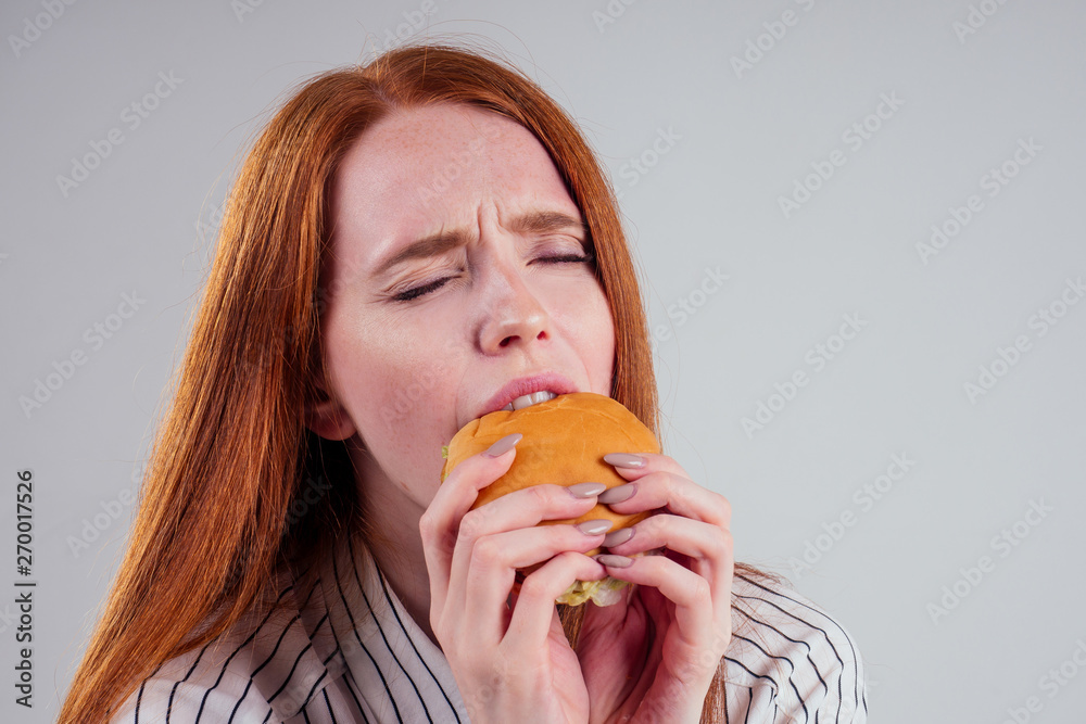 redheared hungry woman in striped shirt eating USA burger visa traveler white background studio redheared hungry woman in striped shirt eating USA burger visa traveler white background studio