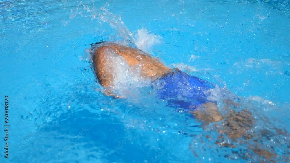 Unrecognizable sporty guy floating across pool with clear blue water. Young man swimming and enjoying recreation on resort in summer sunny day. Concept of vacation or holiday. Side view Slow motion Unrecognizable sporty guy floating across pool with clear blue water. Young man swimming and enjoying recreation on resort in summer sunny day. Concept of vacation or holiday. Side view Slow motion