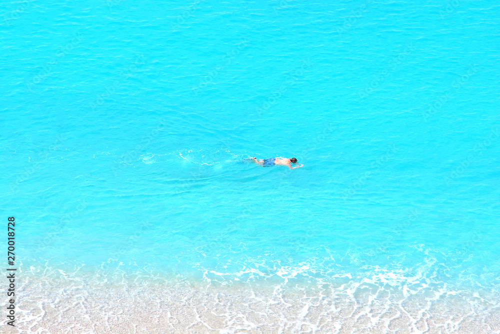 Man swims in the sea with a mask and snorkel. View from mountain.