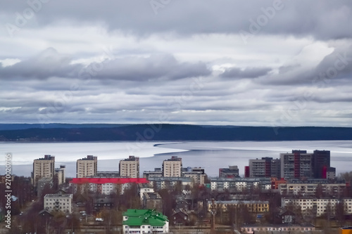 Dramatic dark clouds over a half ice covered lake. View of the city and the lake from a high point.