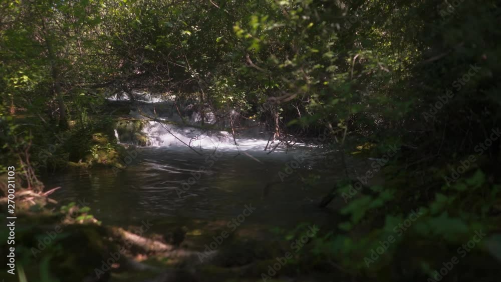 Low angle push through woodland foliage to view of flowing, cascading clean fresh creek waters flowing through Krka national park scenery. Low angle push through woodland foliage to view of flowing, cascading clean fresh creek waters flowing through Krka national park scenery.