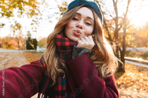 Beautiful happy young pretty woman walking outdoors in autumn spring park take a selfie by camera. photo