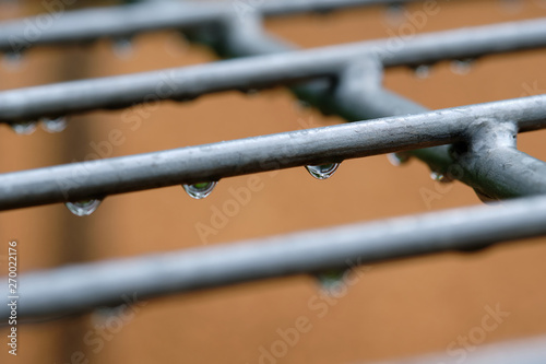 Raindrops hanging on a gray iron grid of a soccer goal on a playground with a brown background