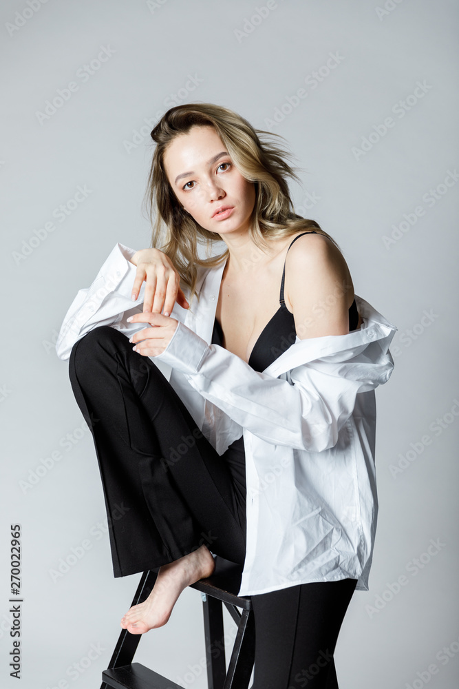 Fashion model sitting on a chair in a white blouse and flared pants barefoot on a white background Fashion model sitting on a chair in a white blouse and flared pants barefoot on a white background