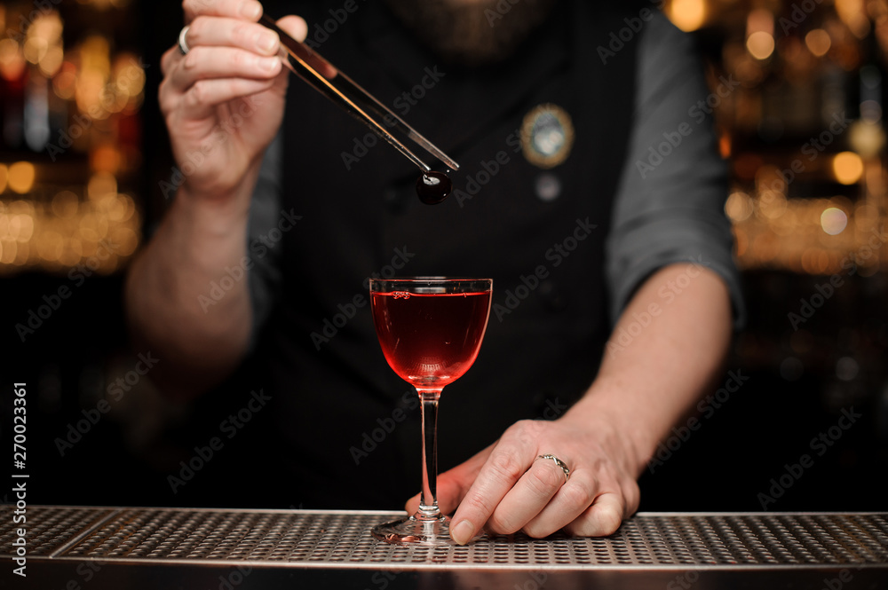 Bartender adding a one red berry with tweezers to the cocktail