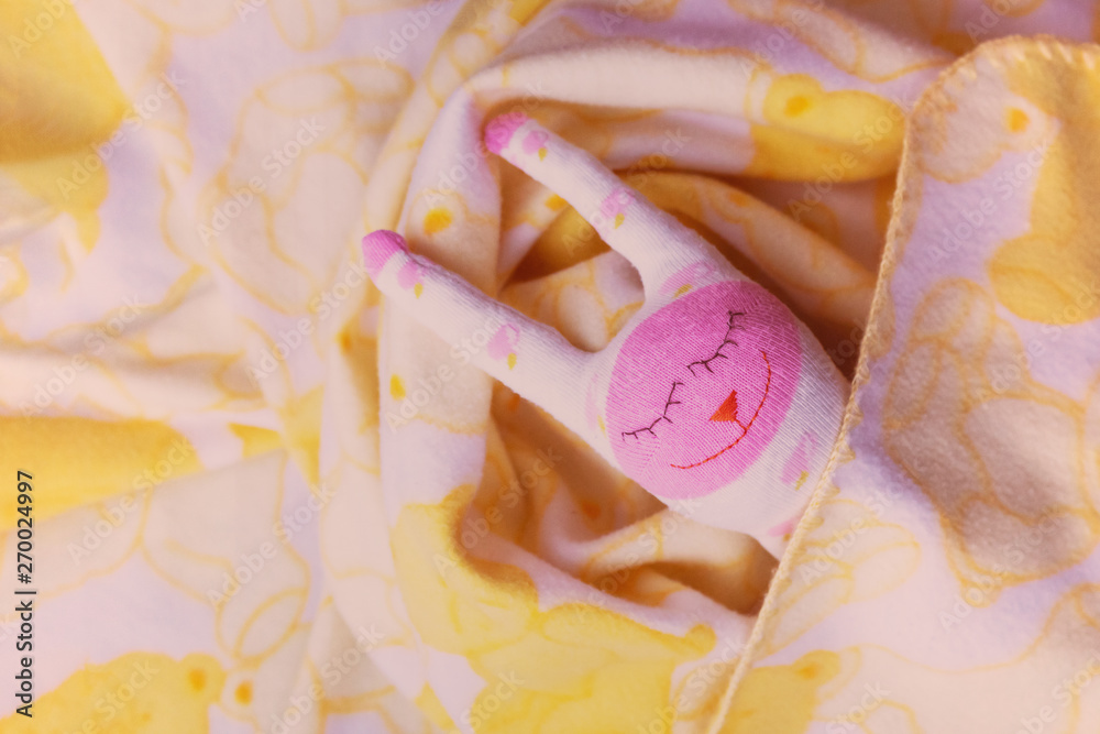 A white, pink toy, a cute hare is lying under a blanket. A white, pink toy, a cute hare is lying under a blanket.