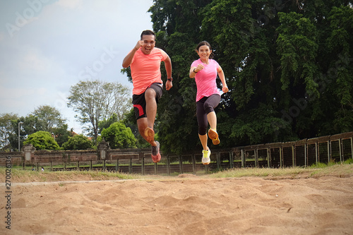Two sports partners are jogging together on a sunny day wearing orange and pink shirts. They jumped and smiled at each other. They are very passionate and enjoy the sports they do