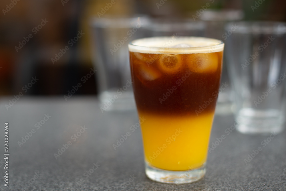 cold brew coffee with orange juice. Glass with cold coffee and ice on the street cafe background. Selective focus