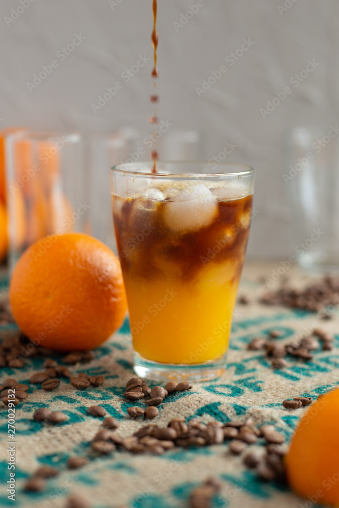 cold brew coffee with orange juice. Glass with cold coffee and ice on the background of a bag and chaotically scattered coffee beans and orange. Selective focus cold brew coffee with orange juice. Glass with cold coffee and ice on the background of a bag and chaotically scattered coffee beans and orange. Selective focus