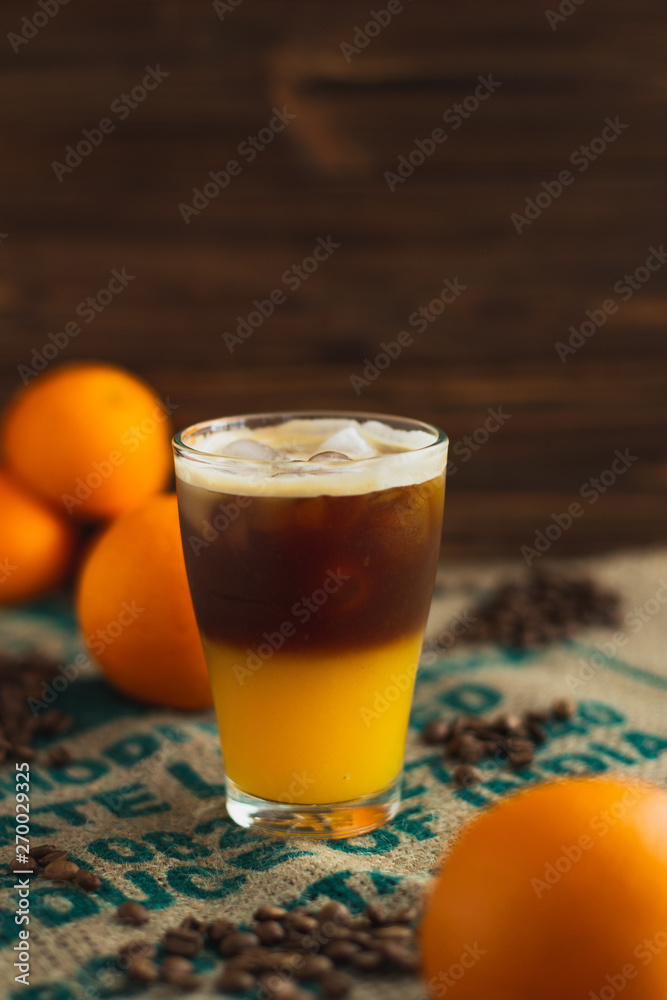 cold brew coffee with orange juice. Glass with cold coffee and ice on the background of a bag and chaotically scattered coffee beans and orange. Selective focus cold brew coffee with orange juice. Glass with cold coffee and ice on the background of a bag and chaotically scattered coffee beans and orange. Selective focus