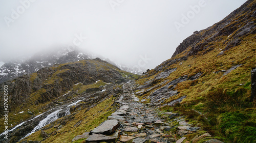 Stunning landscape with foggy skies, melting ice and rugged road among beautiful mountains – captured during a hike at Snowdon in winter (Snowdonia National Park, Wales, United Kingdom)