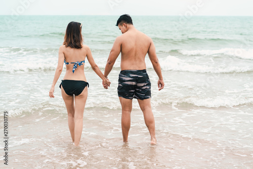 Happy young couple in love holding hands and walking on tropical beach in summer holiday