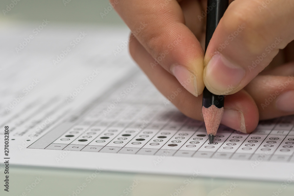 Student hand filling out in answer sheet with standardized test form. - obrazy, fototapety, plakaty 