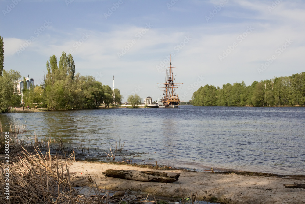 Cityscape, wide river, beautiful embankment, old wooden ship.  City in the distance, across the river.