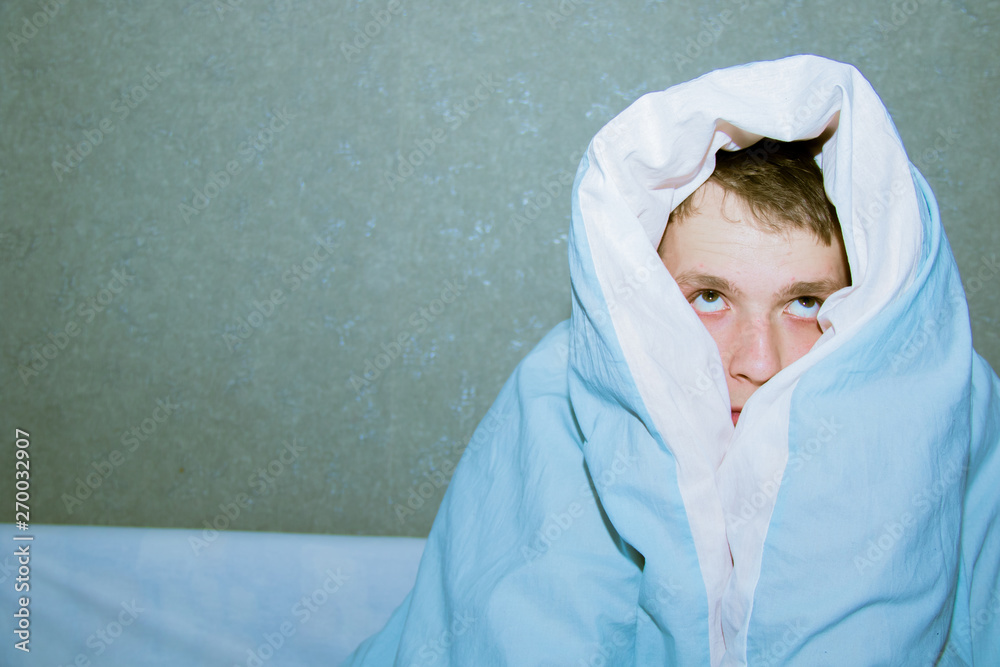 young guy sitting on a bed wrapped in a blue blanket young guy sitting on a bed wrapped in a blue blanket