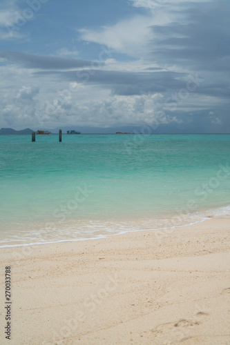 View from the beach on wooden piles in crystal clear sea water over boats and cloudy sky background
