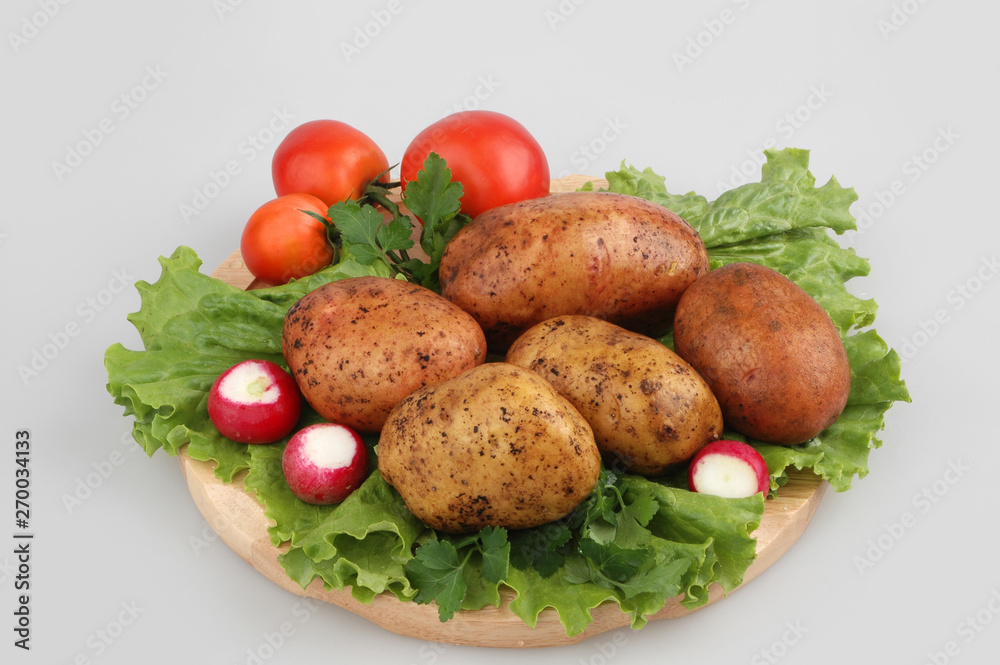 Lots of raw potatoes on wood board with radish, tomatoes, oak lettuce, on gray isolated background