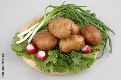 Lots of raw potatoes on wood board with radish, onion, oak lettuce, on gray isolated background