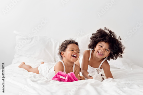 Two little girls laughing together on white bed