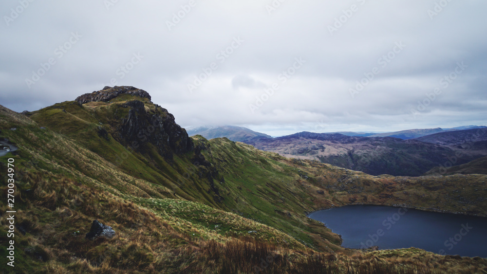 Stunning mountain view from the top seeing a lake, rugged valley and moody skies – captured during a hike at Snowdon in winter (Snowdonia National Park, Wales, United Kingdom) Stunning mountain view from the top seeing a lake, rugged valley and moody skies – captured during a hike at Snowdon in winter (Snowdonia National Park, Wales, United Kingdom)