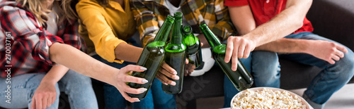 Cropped view of four multiethnic friends with bottles of beer spending time together in living room