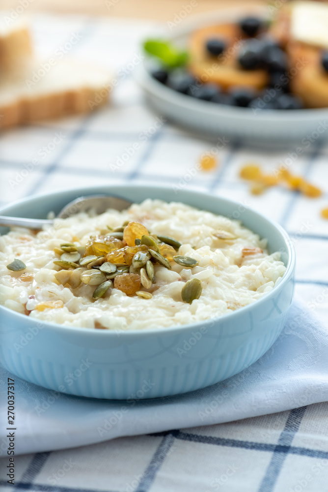 Sweet rice porridge, pudding, with raisins and pumpkin seeds in a blue bowl on the table. Delicious country breakfast. Sweet rice porridge, pudding, with raisins and pumpkin seeds in a blue bowl on the table. Delicious country breakfast.