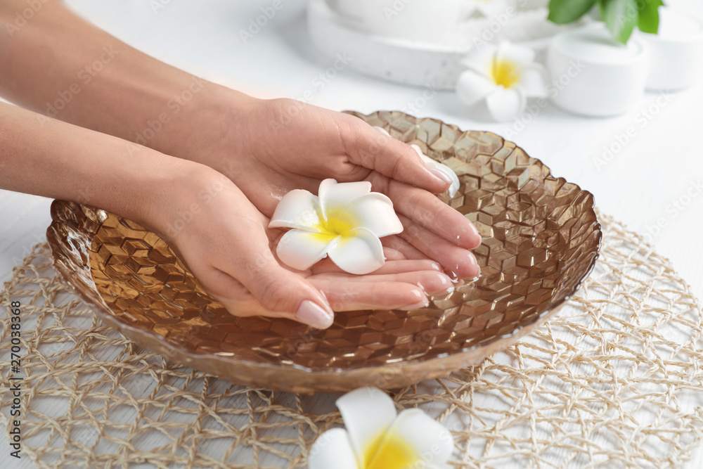 Woman soaking her hands in bowl with water and flowers on table, closeup. Spa treatment Woman soaking her hands in bowl with water and flowers on table, closeup. Spa treatment