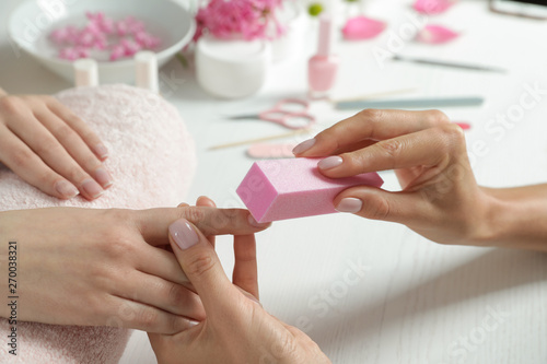 Fotografija Manicurist polishing client's nails with buffer at table, closeup