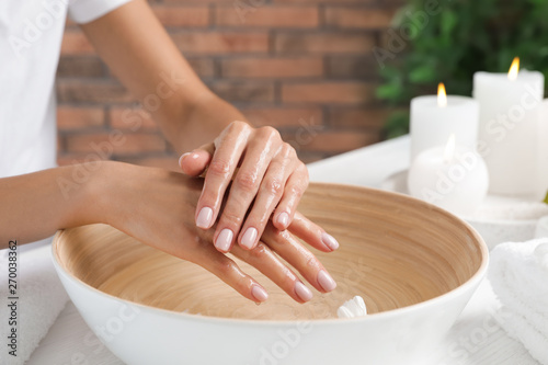 Woman soaking her hands in bowl of water and flowers on table, closeup with space for text. Spa treatment