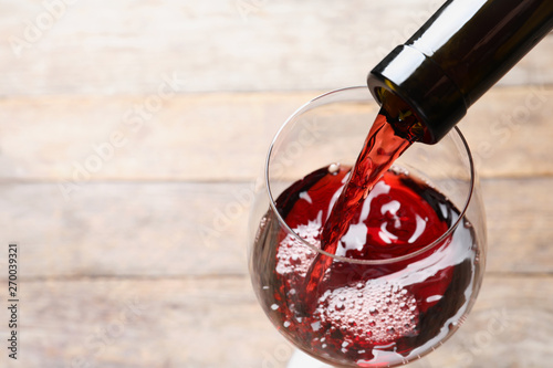 Pouring red wine from bottle into glass on blurred background, closeup. Space for text