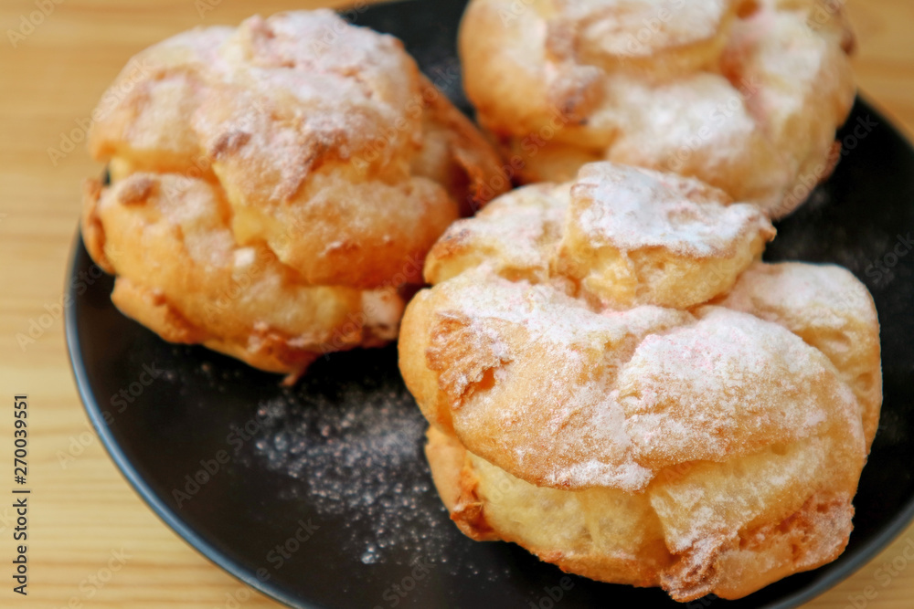 Closeup French Cream Puffs on Black Plate Sprinkled with Icing Sugar
