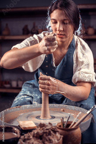 Beautiful artisan woman working on potter's wheel with raw clay with hands. Folk craft. photo