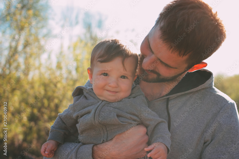 Fototapeta premium Cute baby boy on his dad's shoulders walking on road outdoors, sensitivity to nature concept
