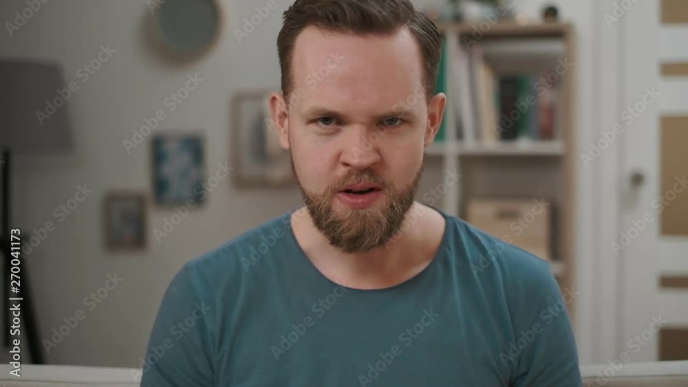 Portrait of angry man displeased and fearful doing disgust face because aversion reaction, annoyance guy sitting on a sofa at home. motional guy disgusted expression, feeling angry, indoor.