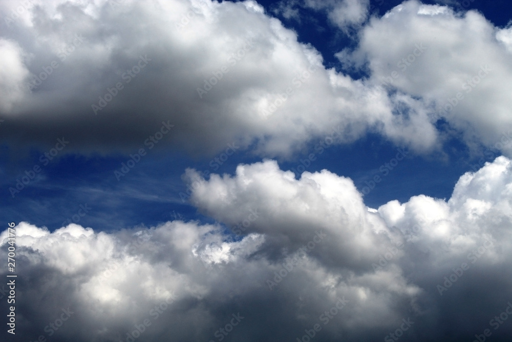 Fototapeta premium White fluffy clouds float above the blue sky, periodically closing the sun