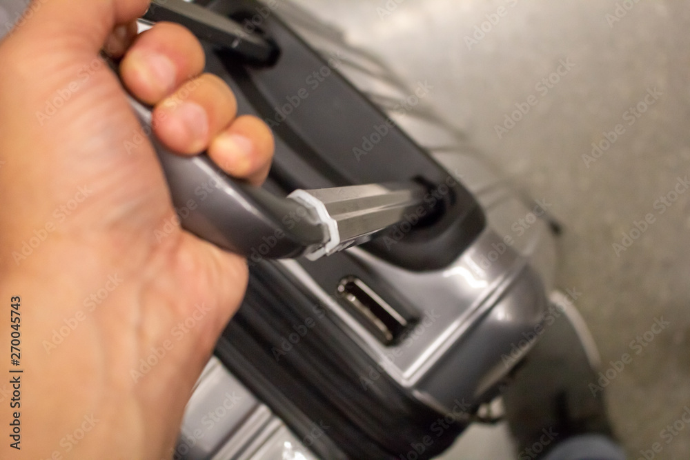 A hand holds onto a rolling compact suitcase at the airport