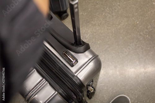 A hand holds onto a rolling compact suitcase at the airport