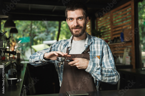 Portrait of attractive barista man making coffee while working in street cafe or coffeehouse outdoor