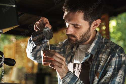 Image of masculine barista man making coffee while working in cafe or coffeehouse outdoor