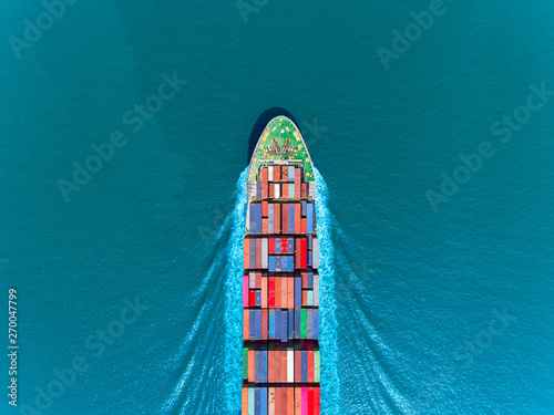 Aerial top view container ship full speed with beautiful wave pattern on the blue sea for logistics, import export, shipping or transportation. © Pawinee