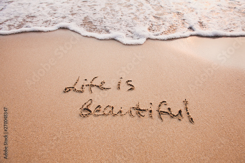 Life is beautiful, positive thinking concept. Inspirational quote written on sand.