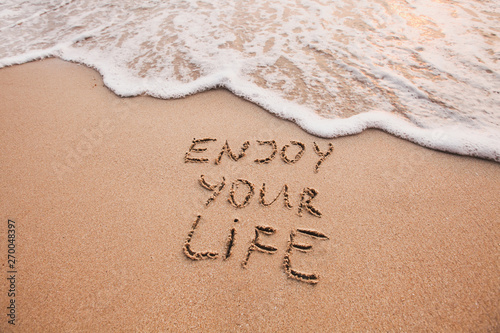 Enjoy your life, happiness concept, positive thinking, inspirational quote written on sand beach.