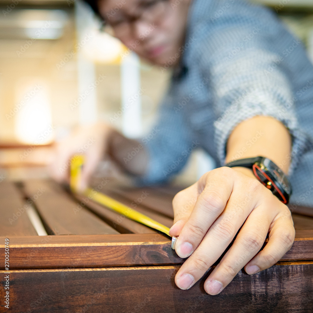 Obraz premium Young Asian man using tape measure for measuring wooden outdoor table in showroom. Shopping furniture for home improvement. Interior design concept